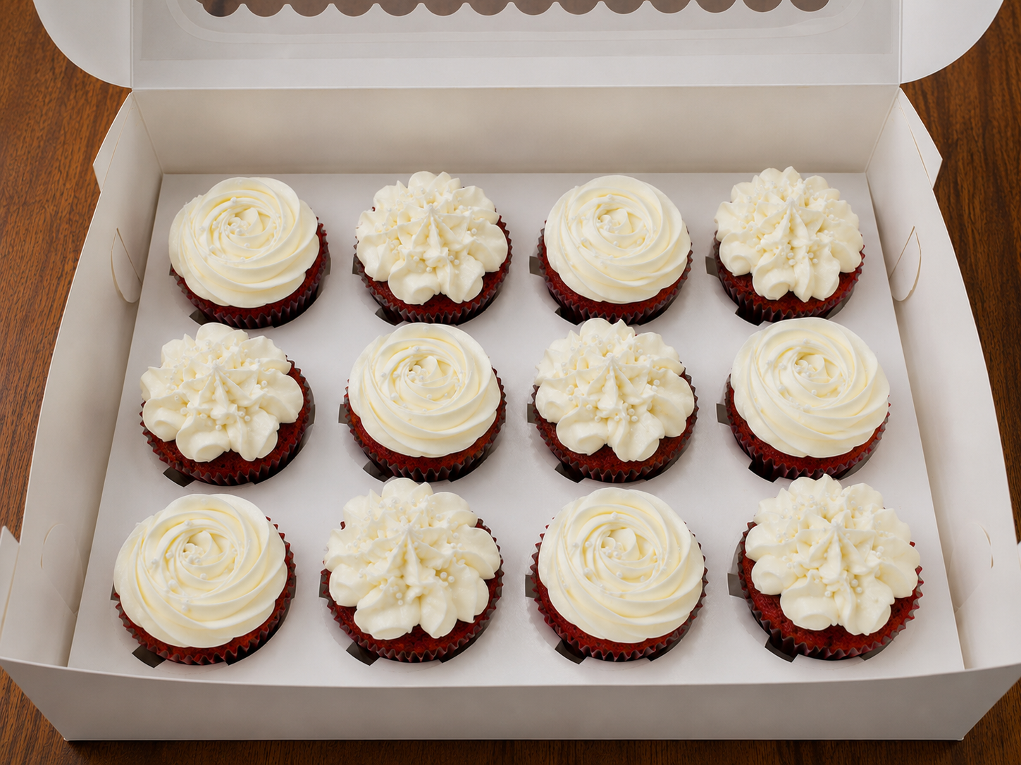 Boxed dozen of red velvet cupcakes topped with whipped cream cheese frosting in rose and star swirls with white sugar pearls