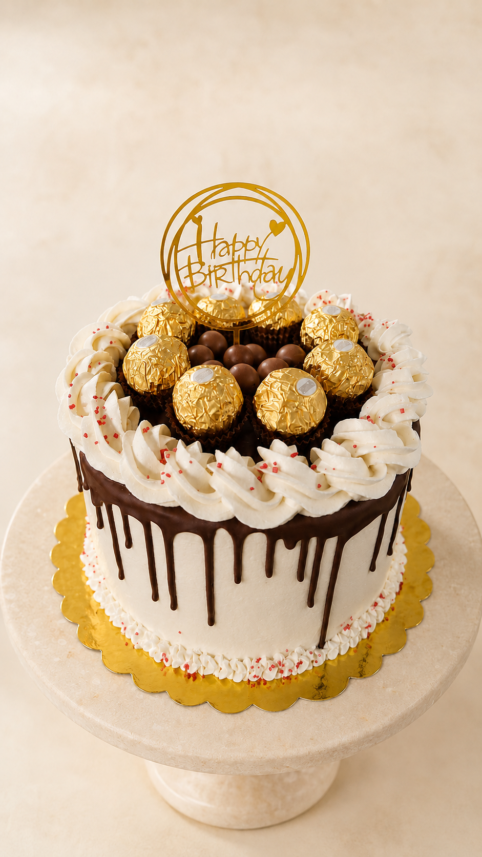 White whipped cream cake with chocolate drip, piped rosette border, red sprinkles and a crown of Ferrero Rocher chocolates and malt balls