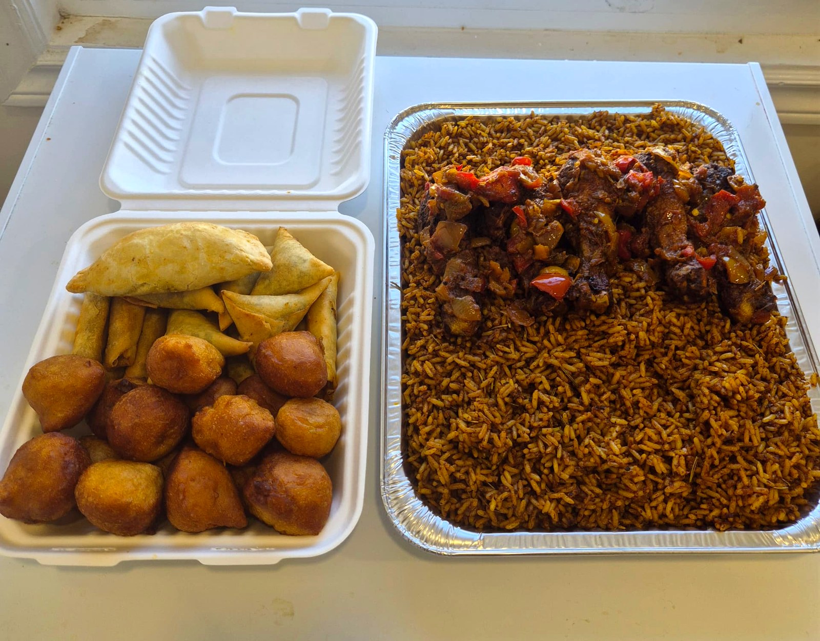 Jollof rice catering tray with peppered meat beside a box of small chops