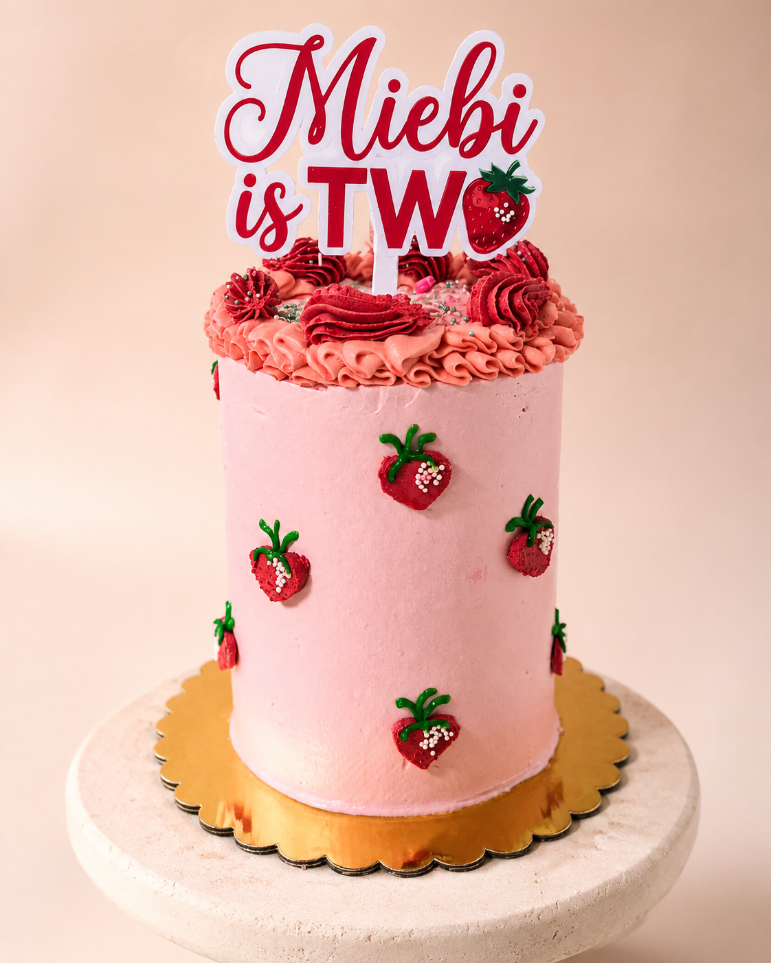 Tall pink strawberry buttercream birthday cake with piped strawberry details and a custom name topper